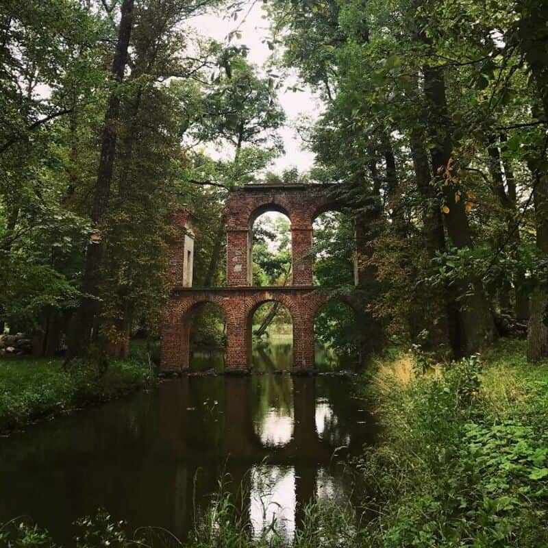 Ruins of an old brick aqueduct over a calm river in a lush forest.