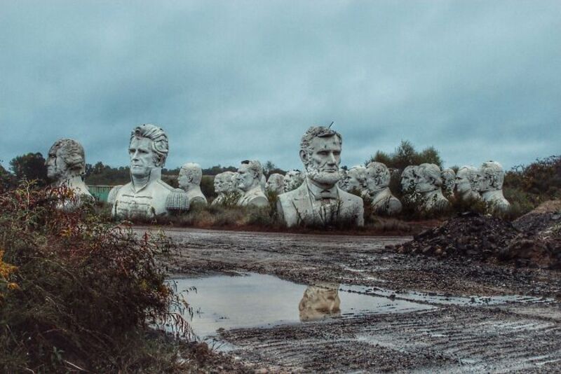 Large stone busts of historical figures in an open field under a cloudy sky.
