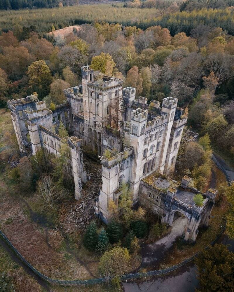 Aerial view of an abandoned castle surrounded by trees in autumn.