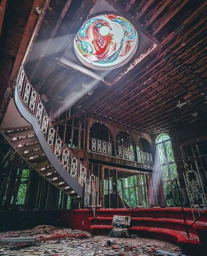 Colorful dragon mural on ceiling of abandoned building with staircase and red carpeted steps.