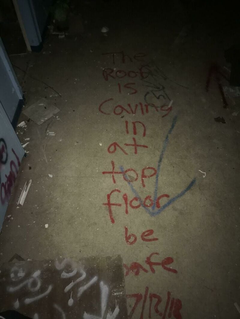 The floor has graffiti that says 'The roof is caving in at top floor be safe'.