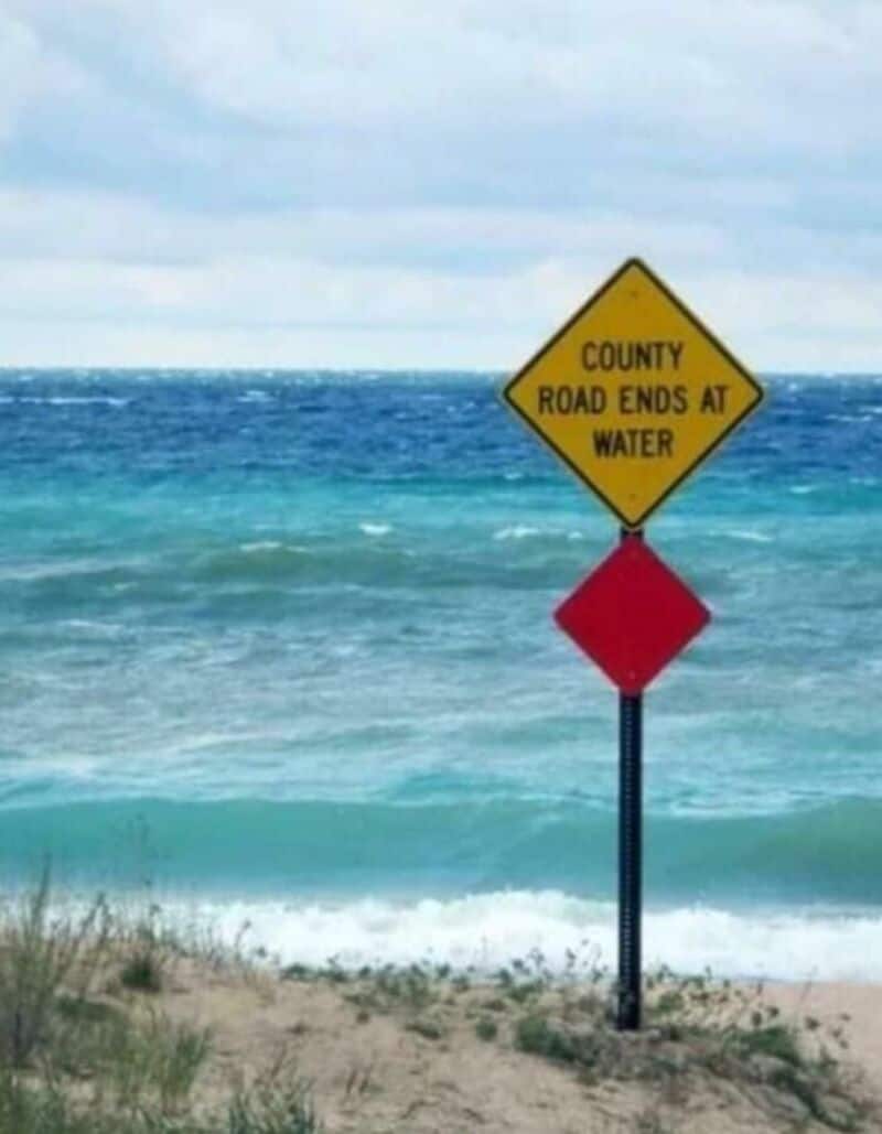 County road ends at water sign on beach with ocean in background.