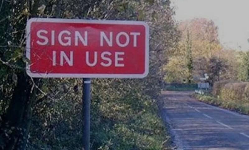 Sign not in use on a rural road with trees and bushes nearby.