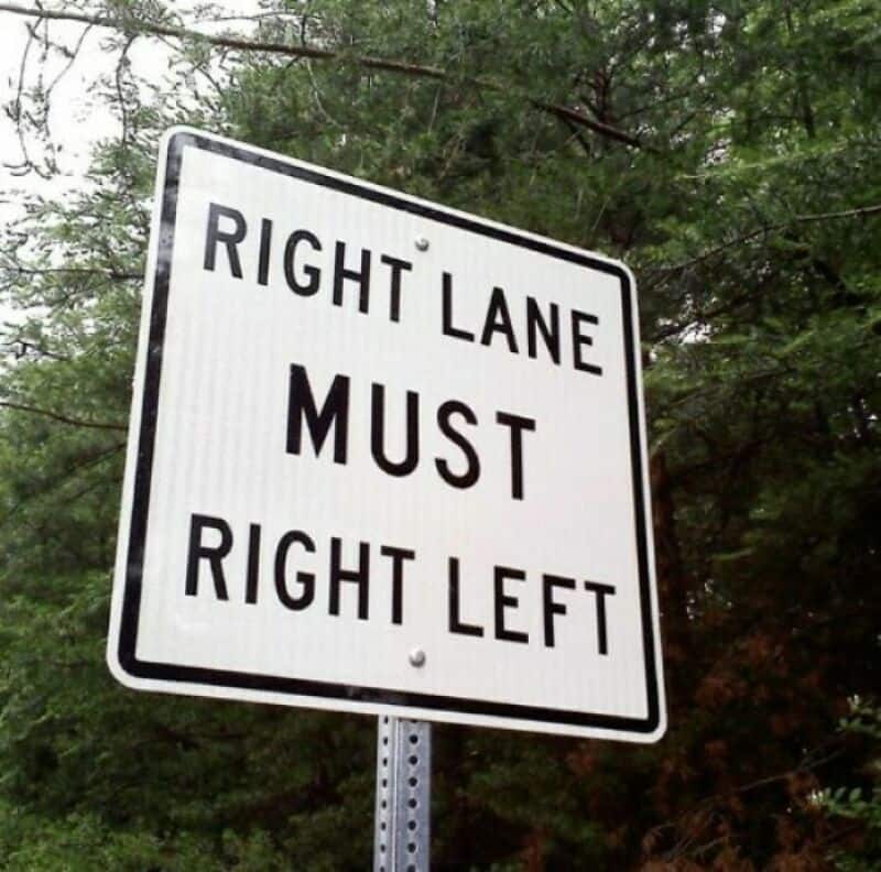 Road sign says 'Right Lane Must Right Left' with trees in background.