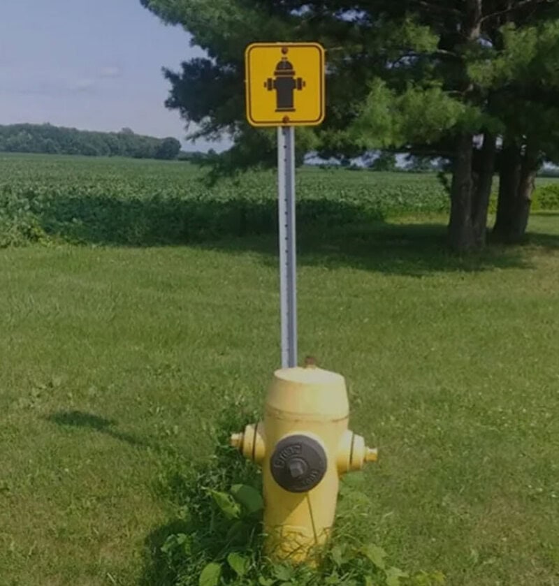 Humorous sign with a firefighter symbol above a fire hydrant in a grassy field.