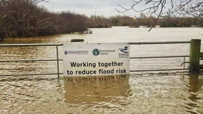 Flooded area with a sign saying 'Working together to reduce flood risk'.