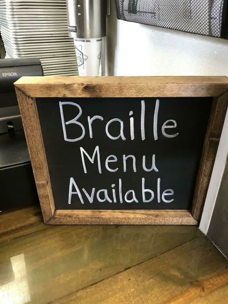 Chalkboard sign reads 'Braille Menu Available' with a humorous typo.