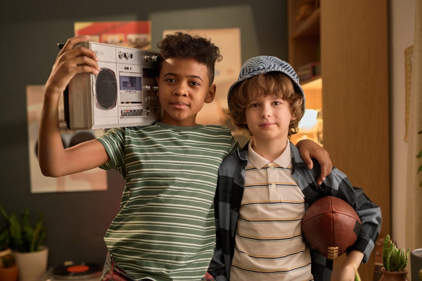Two kids, one holding a boombox, the other with a football, in a cozy room.