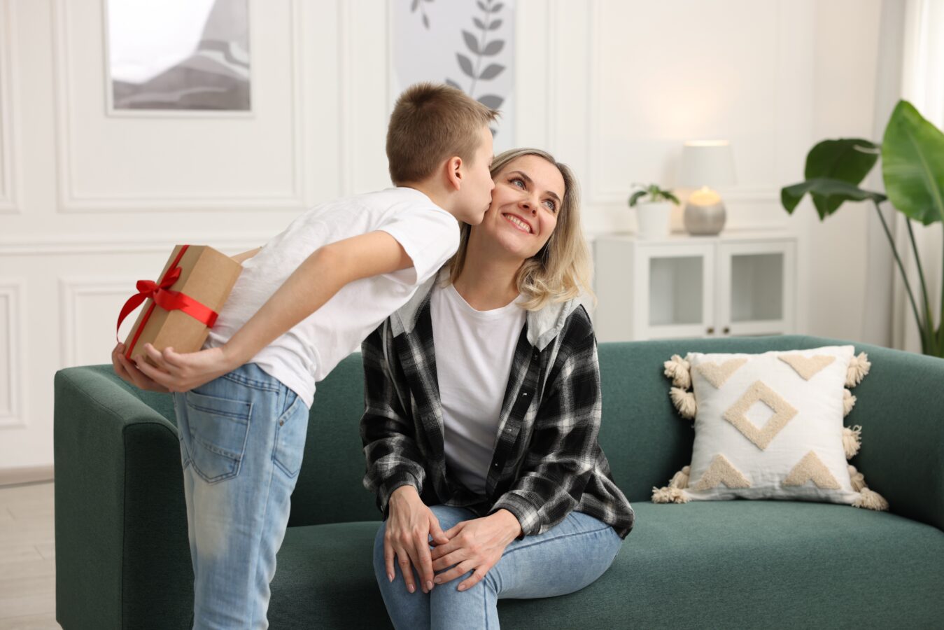 Boy giving a gift to smiling woman on sofa in living room.