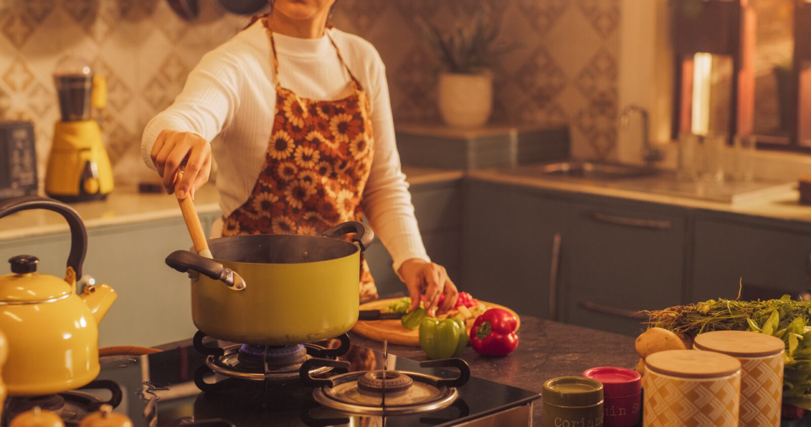 Person cooking in a cozy kitchen with vegetables and a yellow kettle.