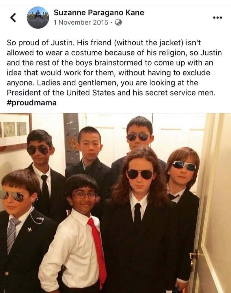 Group of children dressed as adults, wearing suits and sunglasses, in a hallway.