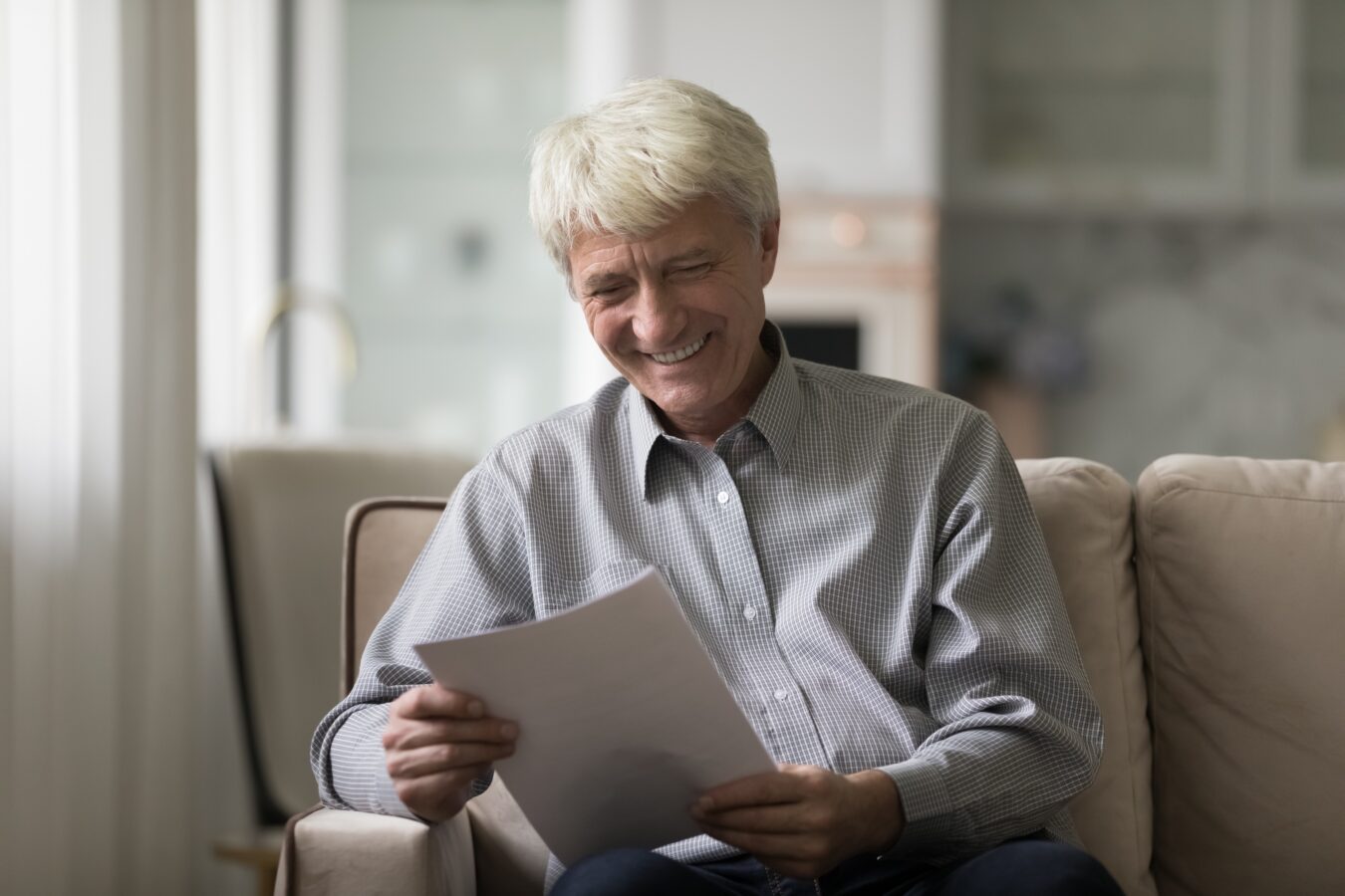 Smiling elderly man reading a letter at home.