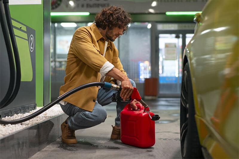 Man refueling car at gas station with a red container nearby.