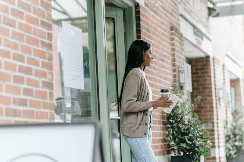 Woman standing outside a cafe holding a coffee and a book.