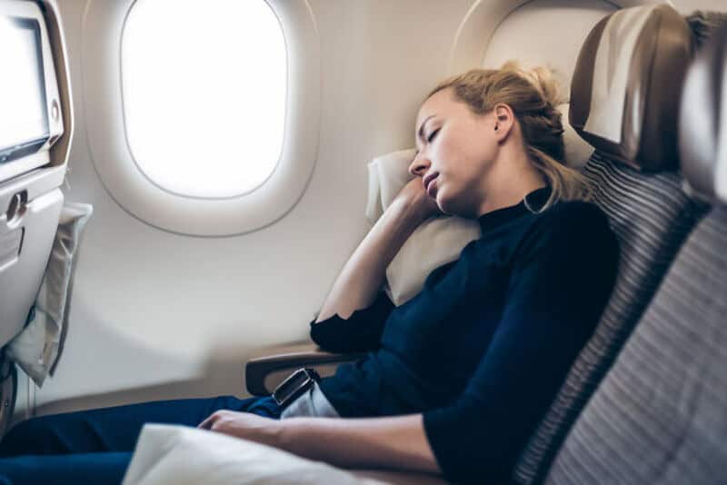 Woman sleeping on airplane seat with window view.