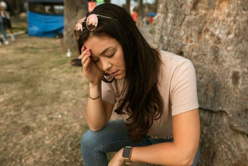 Young woman sitting outdoors, holding her head, looking distressed.