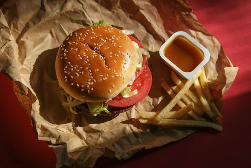 Burger with lettuce, tomato, and sesame seed bun, with fries and dipping sauce.