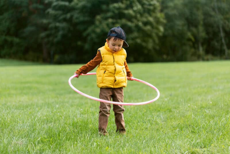 Child playing with a hula hoop in a park during daytime.