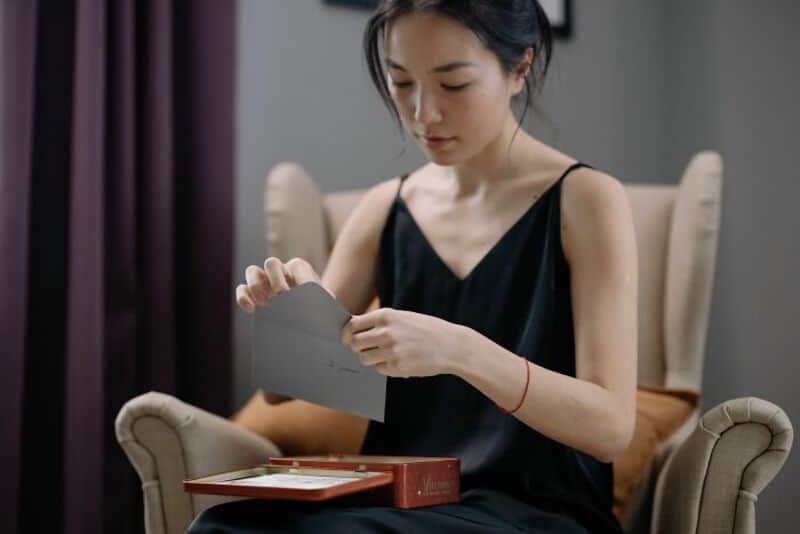 Young woman opening a card or letter while sitting on a beige armchair.