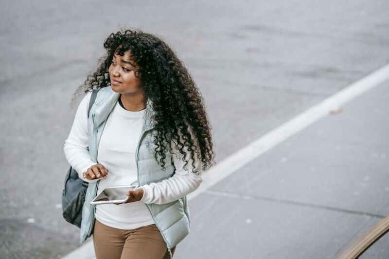 Young woman with curly hair holding a tablet on the street.