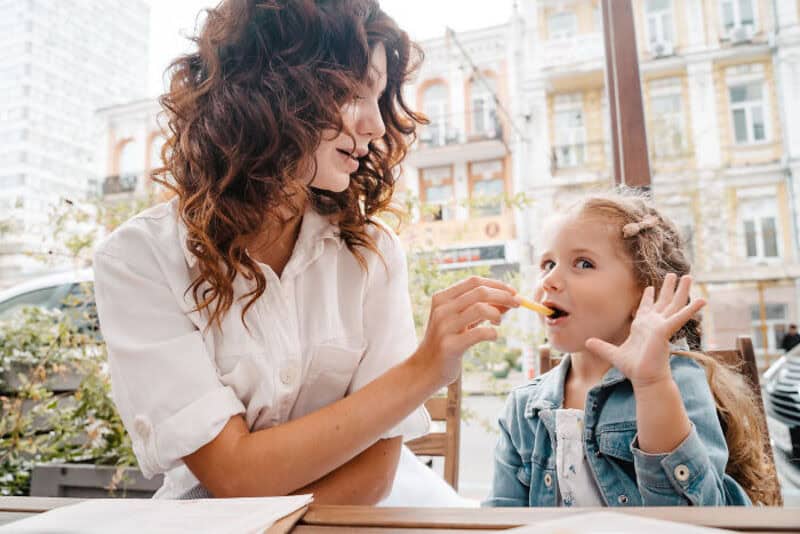 Woman feeding a young girl in an outdoor cafe setting.