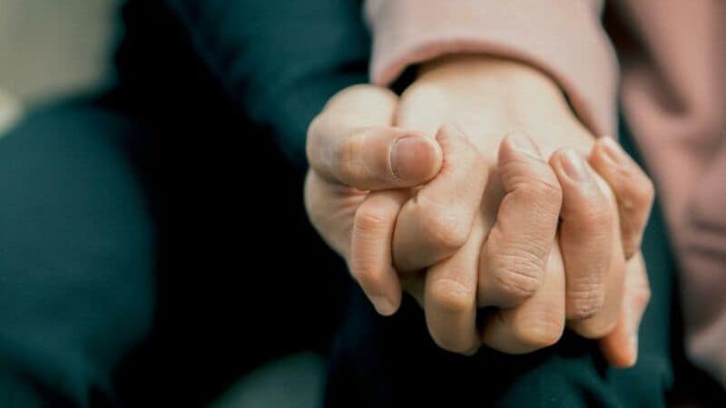 Close-up of two people holding hands, one with a pink sleeve and the other with a dark sleeve.