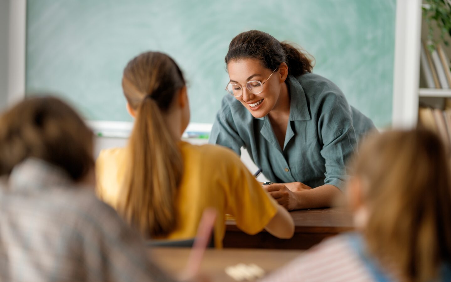 Teacher smiling and talking to students in a classroom.