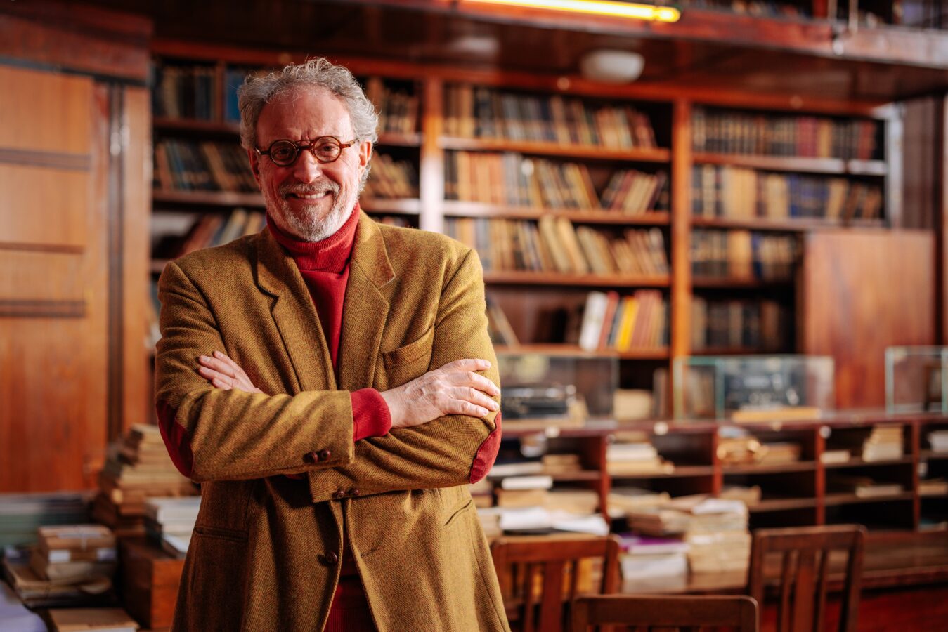 Smiling man with glasses in a library with wooden shelves and books.