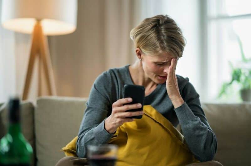 Woman distressed looking at phone, sitting on sofa with yellow pillow.