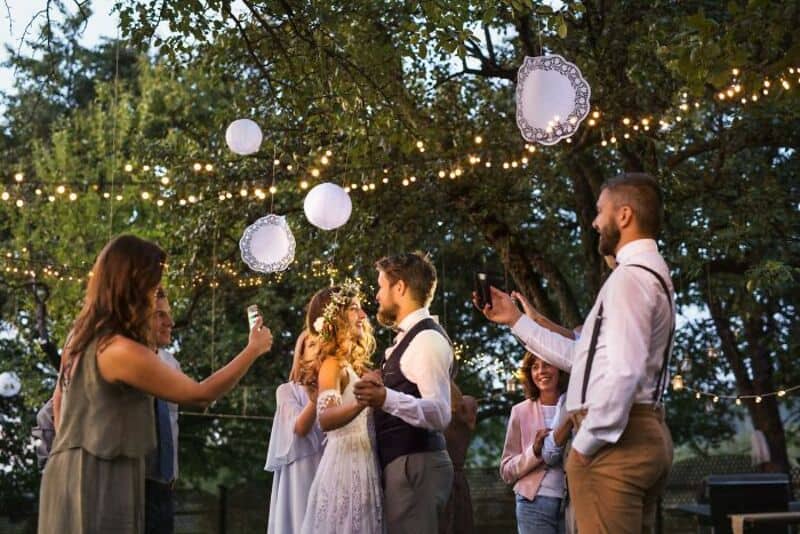 Wedding reception outdoors with string lights, bride and groom, and guests.