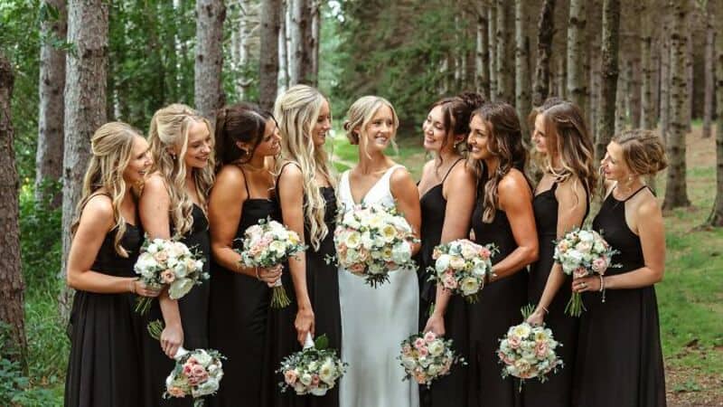 Group of women in black dresses with bouquets in a forest setting.