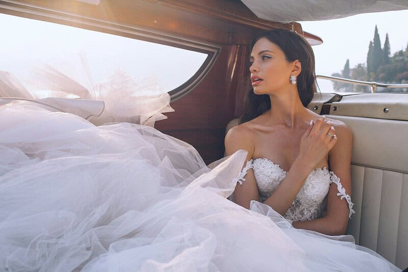 Bride in wedding dress sitting in boat with white tulle and scenic background.