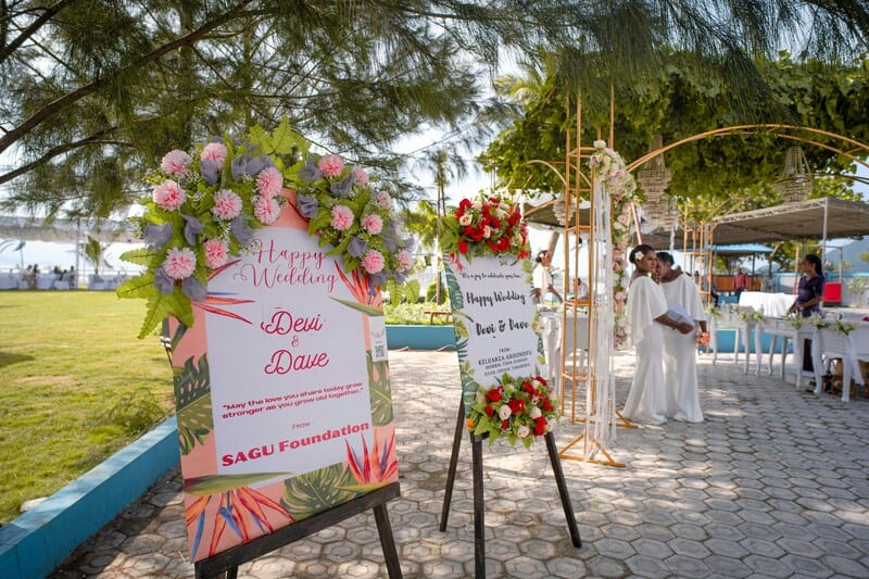 Wedding setup with floral signs and a couple in white dresses under a canopy.