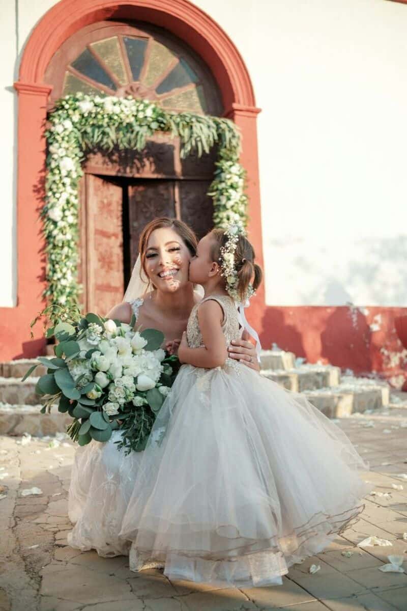 Bride with a young girl kissing her cheek outside a church.