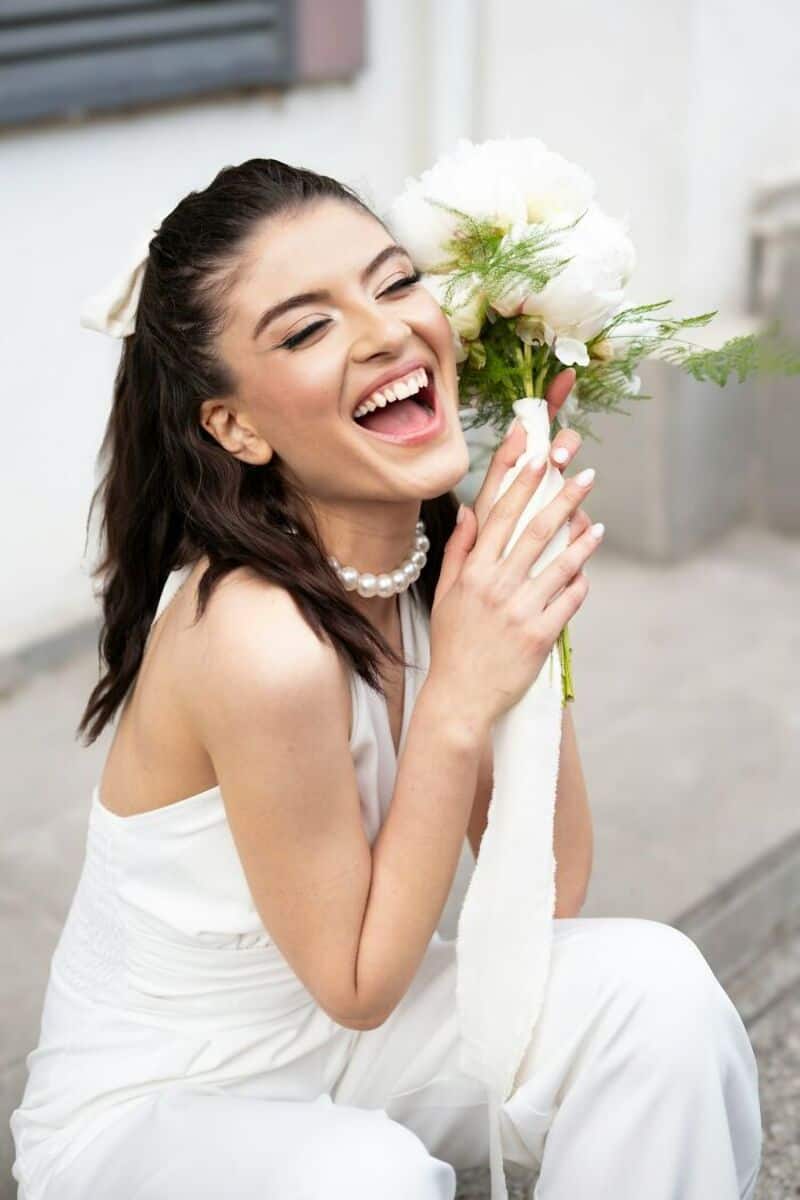 Happy bride holding a bouquet of white flowers, smiling joyfully.