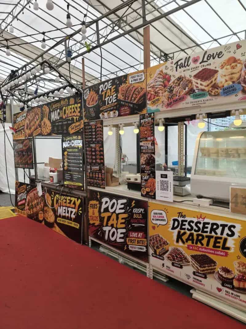 Food stall with signs for cheese, desserts, and snacks in a market setting.