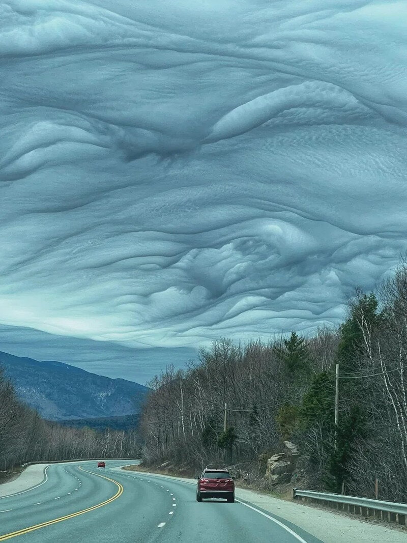 Unusual cloud formation over a mountain road with a car driving beneath.