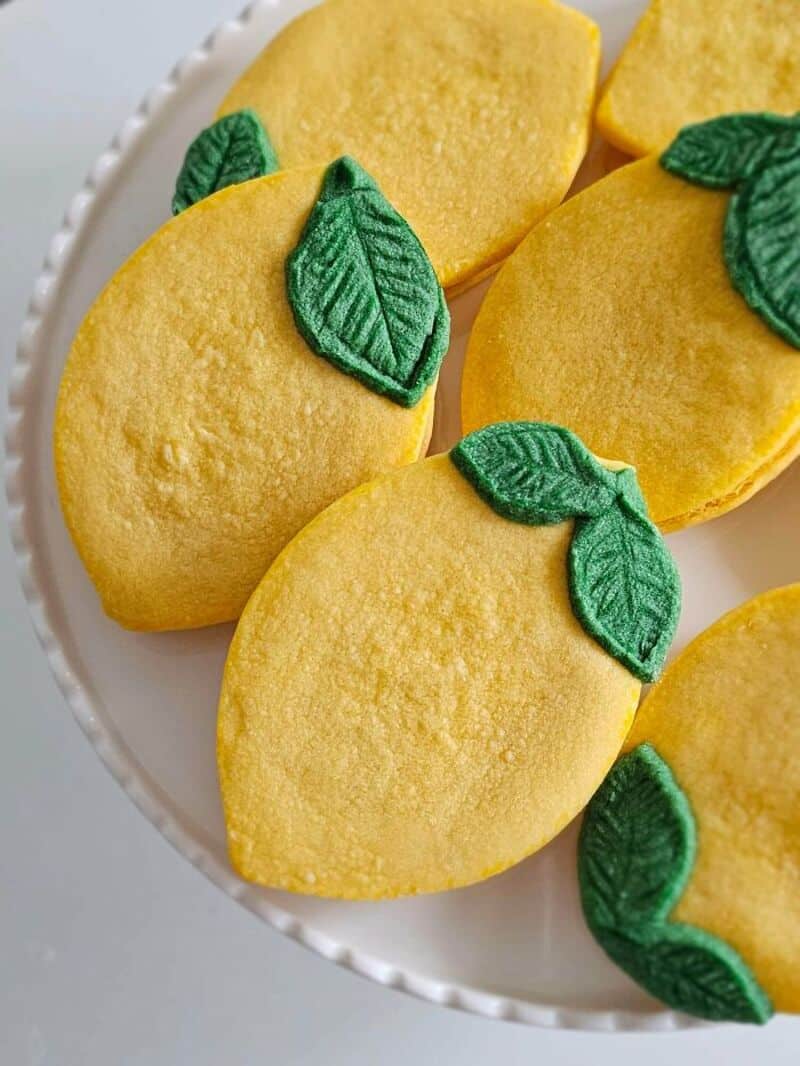 Lemon-shaped cookies with green leaf decorations on a white plate.