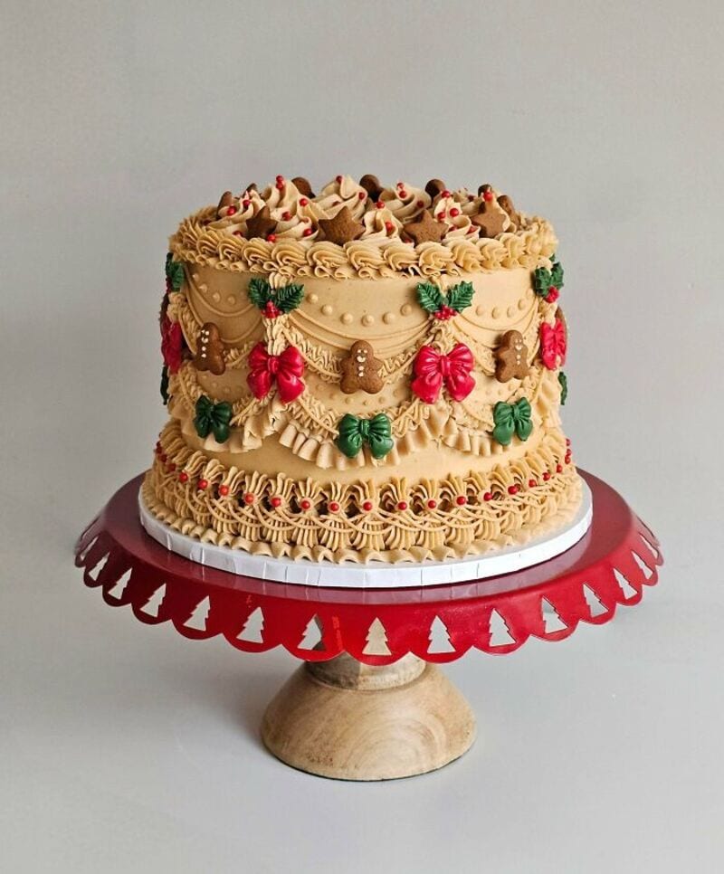 Festive Christmas cake decorated with holly, bows, and gingerbread men on a red cake stand.