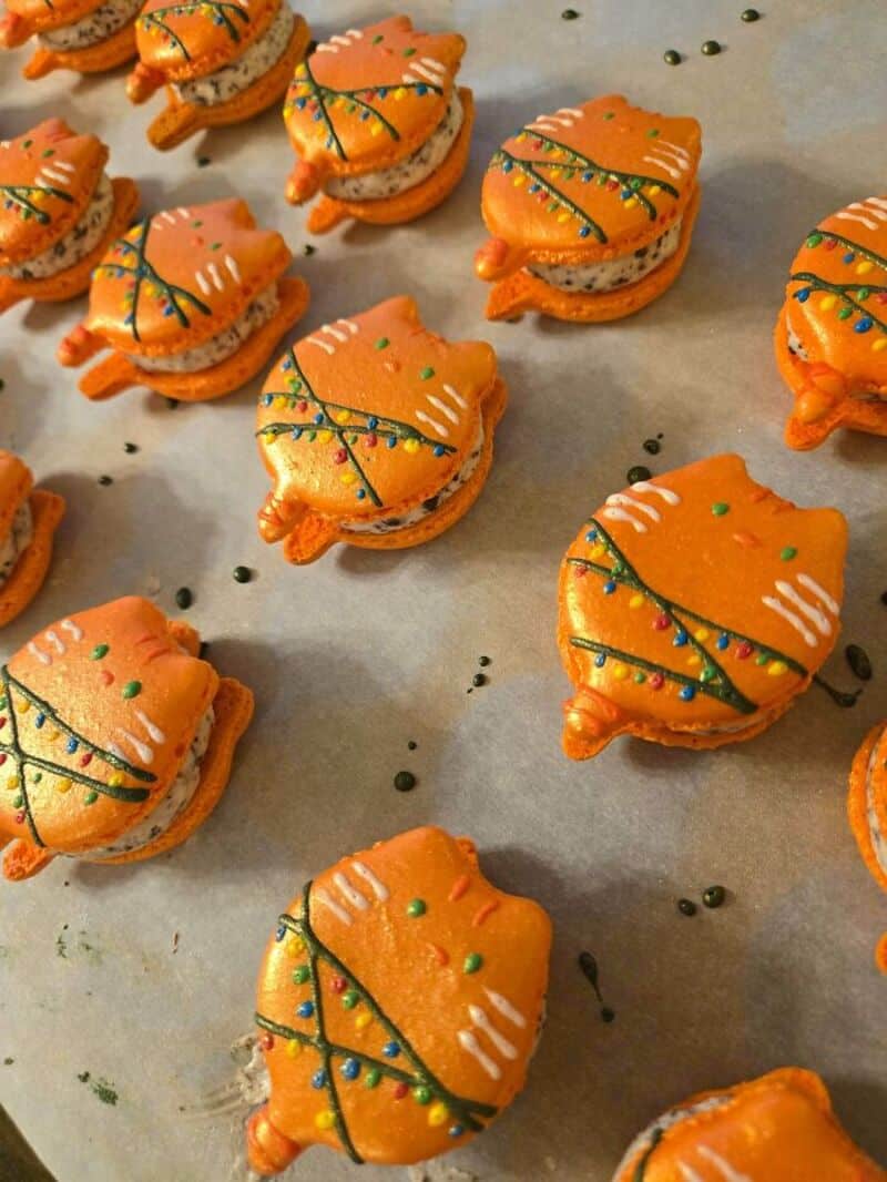 Orange fish-shaped cookies decorated with green and yellow icing, on parchment paper.