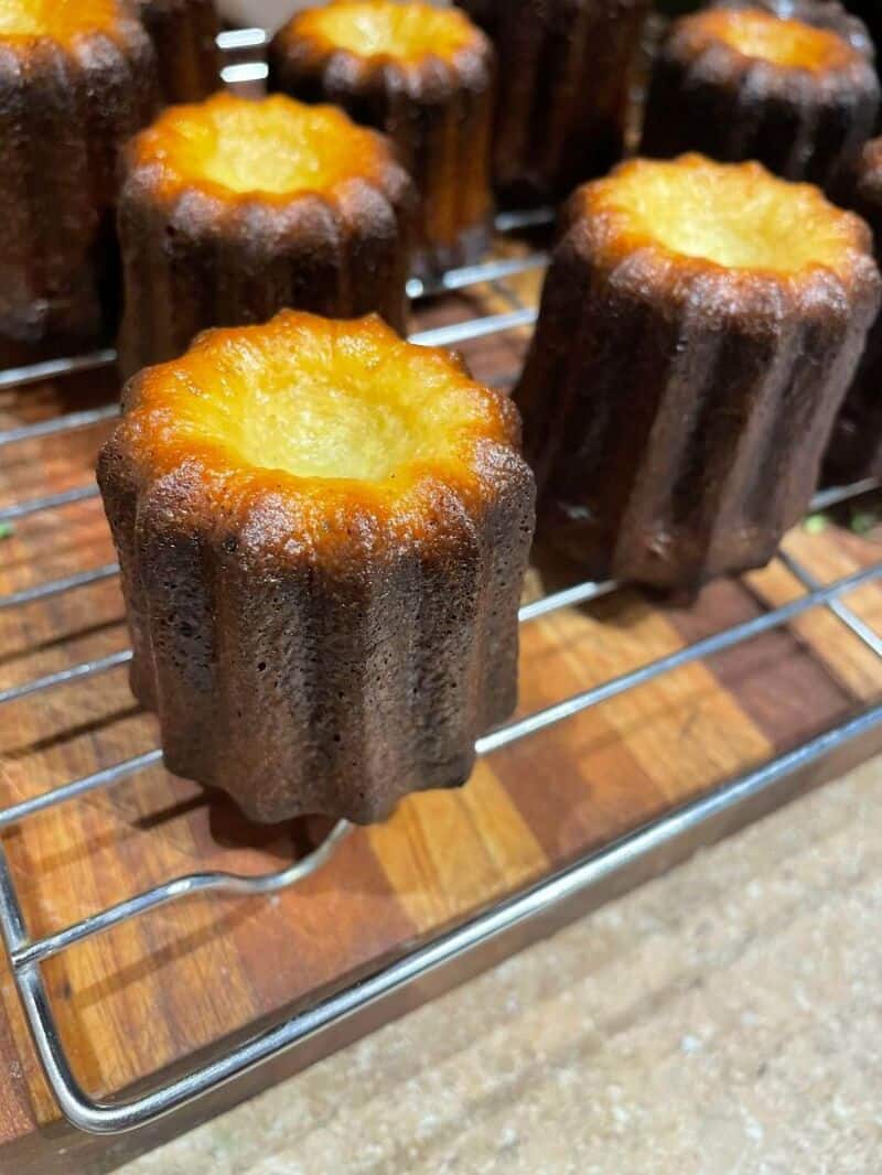 Canelés de Bordeaux on a wire rack, showing their dark caramelized crust and golden interior.