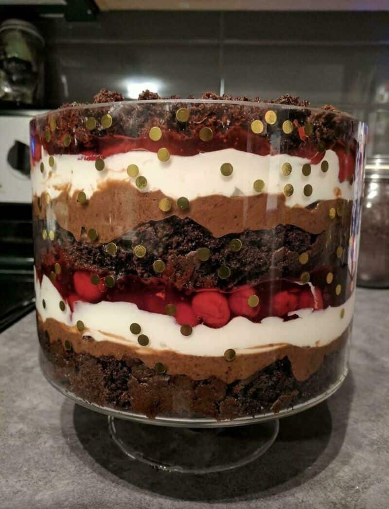 Layered chocolate and berry dessert in a glass bowl with gold sprinkles.
