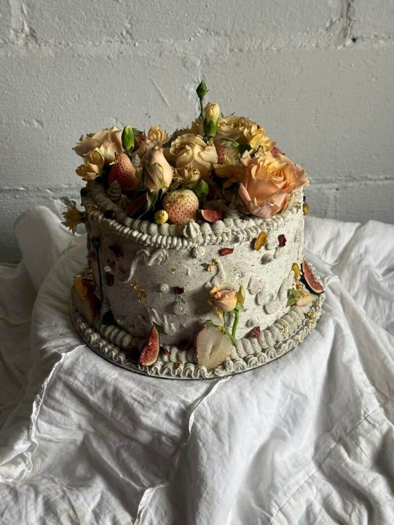 Cake decorated with strawberries, roses, and other flowers on a white cloth.