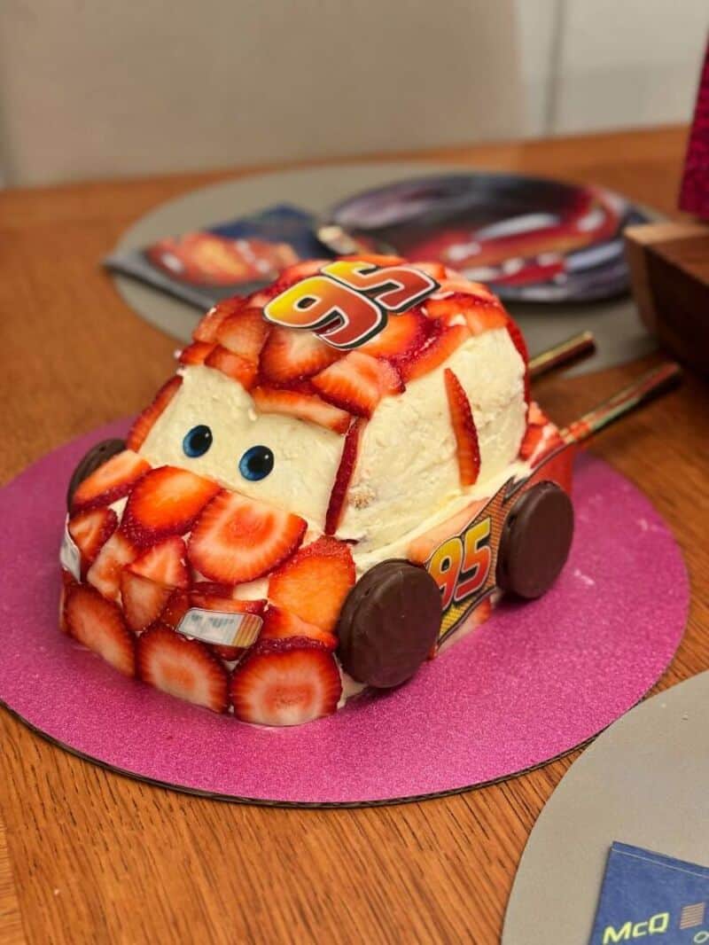 Cake shaped like Lightning McQueen from Cars with strawberries and chocolate details.