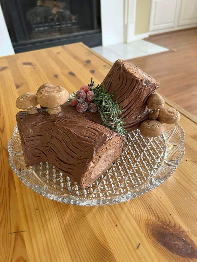 Chocolate Yule log cake with mushrooms and berries on a glass plate.