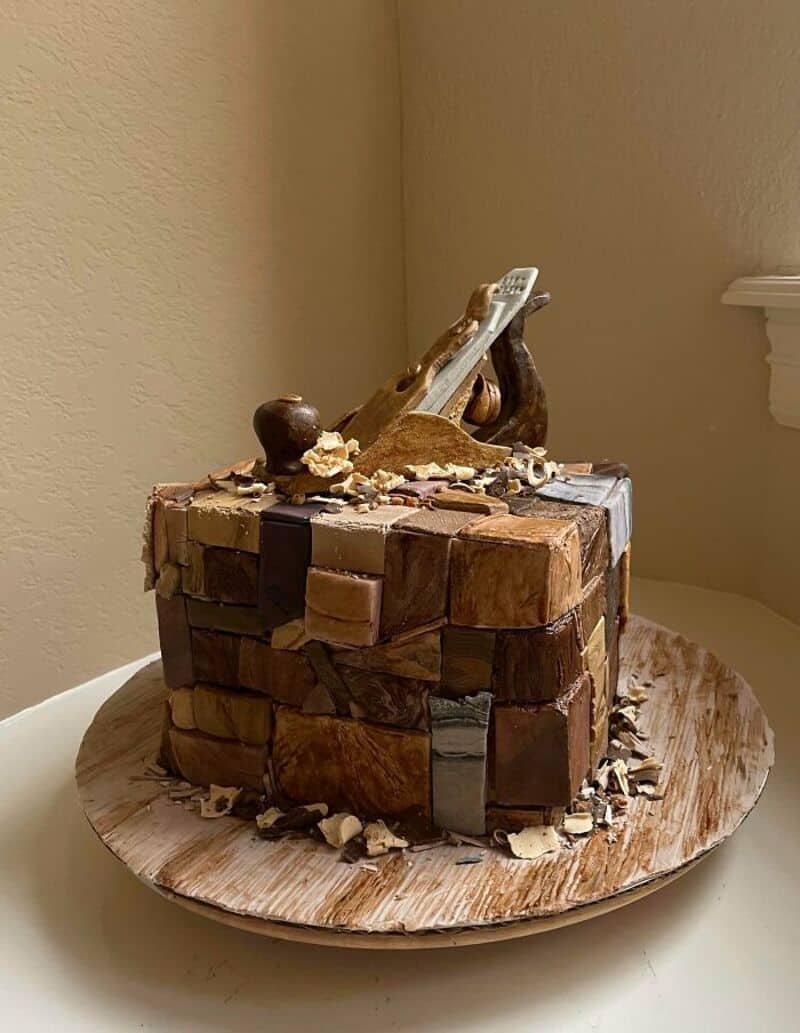 Chocolate and vanilla layered cake with a hammer on top, on a wooden board.