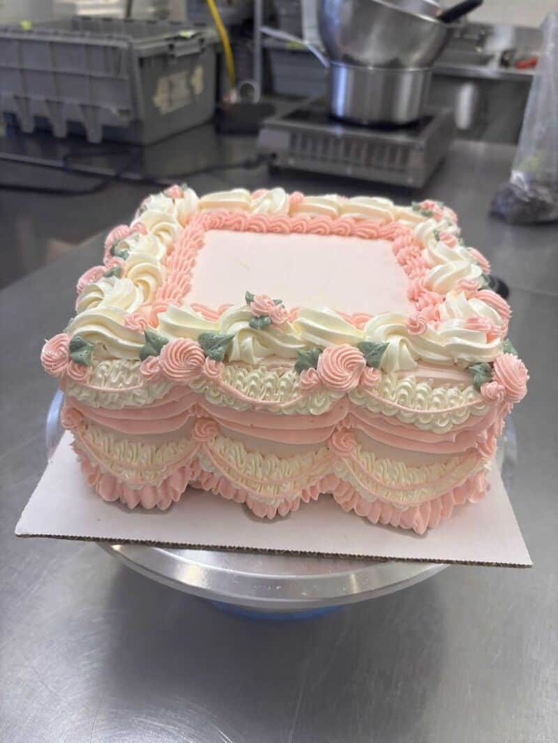 Pink and white decorated rectangular cake with floral patterns on a cake stand.