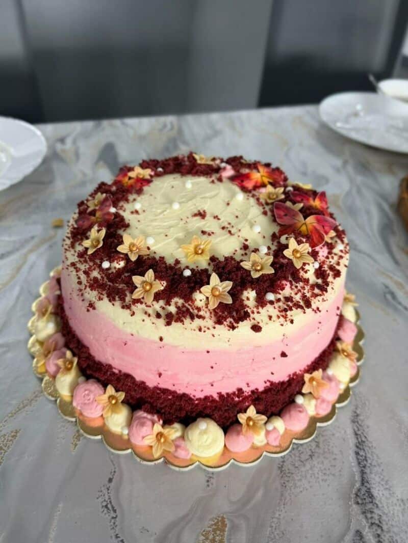 Pink and white layered cake with flower decorations and red sprinkles on top.