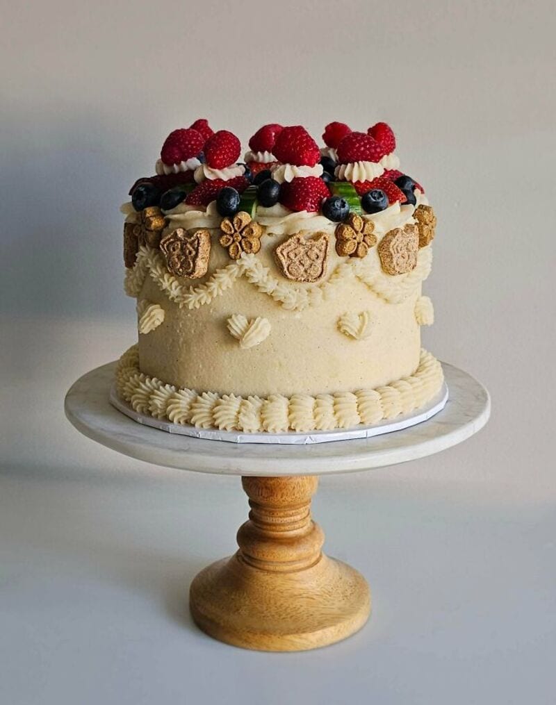 Cake decorated with berries and cookies on a wooden stand.