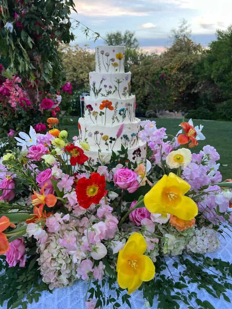 Four-tiered wedding cake with floral decorations, surrounded by colorful flowers.